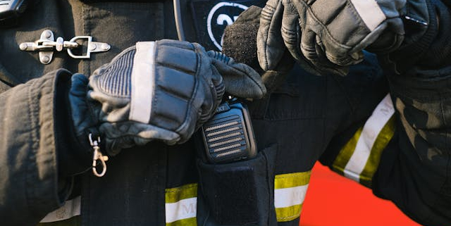 A man wearing a jacket and gloves, is seen putting a two-way radio in his pocket