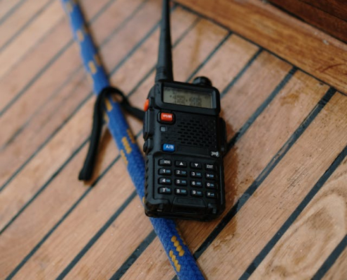 A two-way radio kept on a wooden-top table, nearby a rope