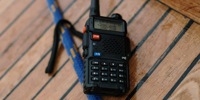 A two-way radio kept on a wooden-top table, nearby a rope