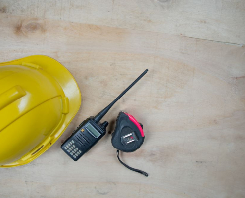 A portable black two-way radio is kept on a table-top, beside a helmet