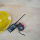 A portable black two-way radio is kept on a table-top, beside a helmet